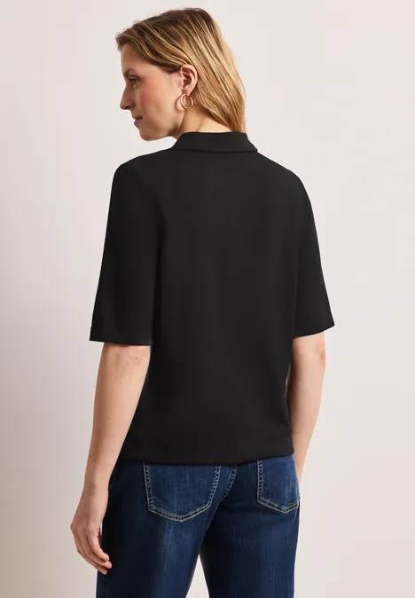 Frau von hinten in schwarz kurzärmeligem Poloshirt und blauer Jeans, Gesicht unscharf.